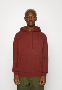 Mörkröd hoodie med en framficka, snörning i huvan och svart Nike-logotyp på bröstet. Har raglanärmar och ribbade muddarmar.