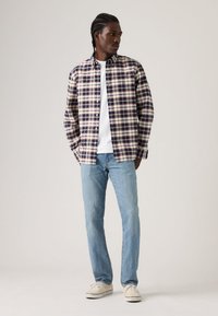 Καρώ πουκάμισο με κουμπιά σε ναυτικό μπλε, κρεμ και βουργουνδί; λευκό μπλουζάκι με στρογγυλή λαιμόκοψη; ανοιχτό μπλε τζιν; casual αθλητικά παπούτσια. Λείο ύφασμα, χαλαρή εφαρμογή.