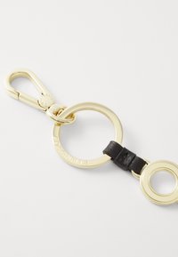 Portachiavi placcato in oro con un grande anello, accento in pelle nera e un gancio sicuro per il fissaggio. Design circolare con branding inciso.