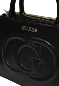 La borsa a mano in pelle nera presenta un logo impresso, hardware dorato e chiusura con zip; texture liscia con forma strutturata e manici arrotondati.