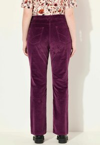 Pantalons en velours côtelé de couleur violet profond avec une coupe droite, dotés de deux poches arrière et d'une finition texturée. Associés à un haut à fleurs.