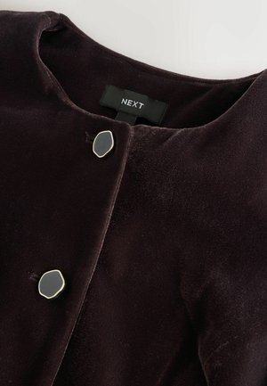 Dunkelviolettes Samtjacket mit rundem Ausschnitt, ausgestattet mit zwei ovalen schwarzen Knöpfen in einer goldenen Fassung, beschriftet mit "NEXT". Glatte Textur.
