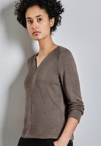 Maglione lavorato a maglia marrone con scollo a V, maniche lunghe e cuciture laterali. Tessuto morbido con un motivo sottile, abbinato a pantaloni neri.