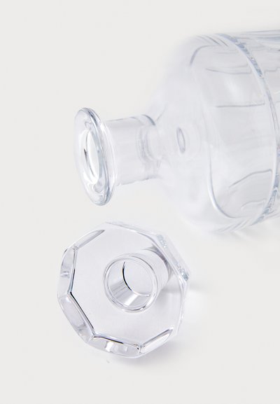 Botella de vidrio transparente con cuello redondeado y tapa octagonal, con una superficie lisa y acabado claro, posicionada en diagonal.