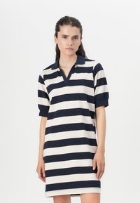 Ριγέ πόλο φόρεμα σε navy και κρέμα, κοντά μανίκια, v-λαιμόκοψη, μαλακό ύφασμα, μέχρι το γόνατο, με έντονες οριζόντιες ρίγες.