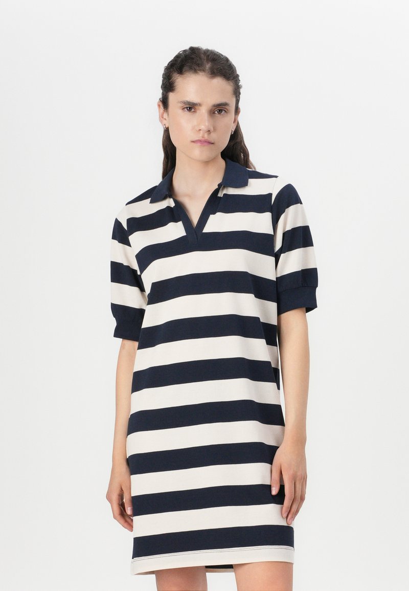 Ριγέ πόλο φόρεμα σε navy και κρέμα, κοντά μανίκια, v-λαιμόκοψη, μαλακό ύφασμα, μέχρι το γόνατο, με έντονες οριζόντιες ρίγες.