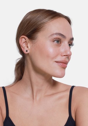 Sorte stiftøredobber vist på en modell med lys hudtone og glatt hår, som fremhever et minimalistisk design og sirkulær form.