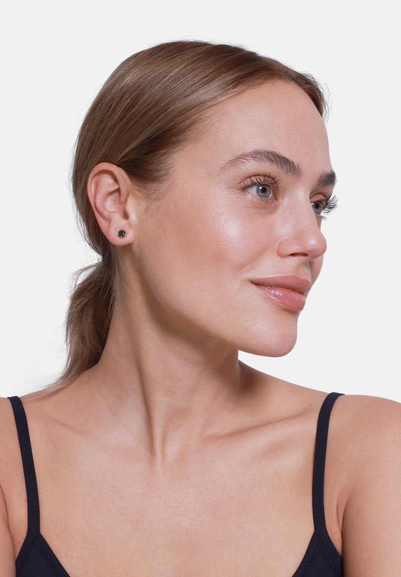 Boucles d'oreilles noires en clou exposées sur un modèle à la peau claire et aux cheveux lisses, mettant en avant un design minimaliste et une forme circulaire.