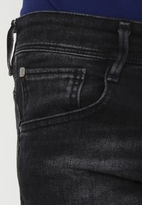 Musta denim-housut slim fit -mallissa, joissa on etutasku ja hillitty haalistuminen. Valmistettu pehmeästä, rakenteellisesta kankaasta, jossa on kestävä ommel.