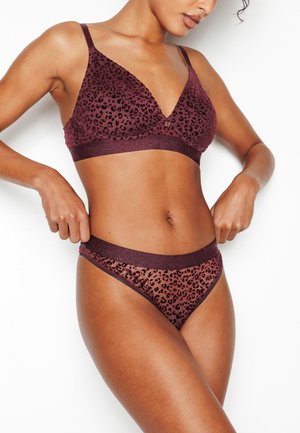 Donna che sistema un completo lingerie color bordeaux con stampa leopardata, composto da reggiseno e mutandine abbinate, su sfondo bianco.
