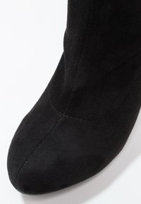 Botín de ante negro hasta el tobillo con punta afilada y diseño sin costuras. Textura suave con un sutil detalle de costura a lo largo de las uniones.