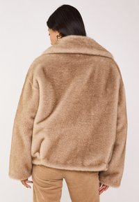 Veste en polaire marron doux et surdimensionnée avec un large col et des poignets côtelés, associée à un pantalon en velours côtelé marron clair.