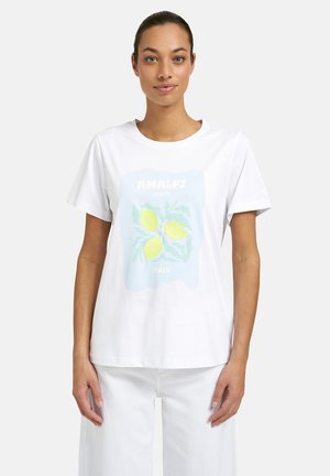 Frau trägt ein weißes T-Shirt mit einem pastellblauen Quadrat, das drei gelbe Zitronen und den Text "Amalfi-Küste Italien" zeigt.
