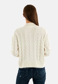 Maglione bianco a trama intrecciata con orlo e polsini a costine, caratterizzato da motivi testurizzati e una vestibilità comoda, abbinato a jeans scuri.