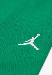 Zelená látka s textúrovanou väzbou má biele vyšívané logo Jumpman v akčnej póze, umiestnené na jednofarebnom pozadí.