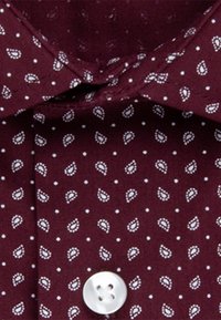 Bordová košile s bílým vzorem paisley a malými tečkami; má klasický límec a jeden bílý knoflík vpředu.