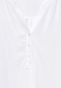 Camisa de algodón blanca con escote en V, cinco botones en la parte frontal y una textura suave y lisa. Sin patrones ni acentos visibles.