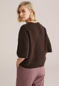 Barna, texturált pulóver laza szabással és rövid ujjal. Széles nyakkivágással rendelkezik, és világos rózsaszín nadrággal van párosítva.