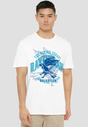 Young man wearing a white T-shirt with a blue raven graphic and the text "Try Flying Today Ravenclaw Quidditch".