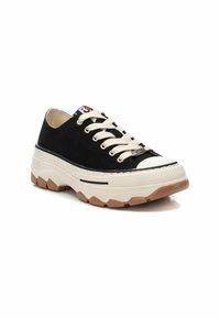 Zapatillas de lona negras con cordones crema, suela intermedia blanca gruesa y suela de goma marrón. Presenta una punta redondeada y costuras en contraste.