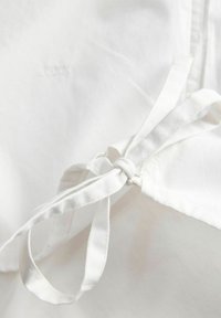 Bijeli platneni pregač vezan u jednostavnu mašnu s vidljivim šavovima na glatkoj tekstilnoj pozadini.