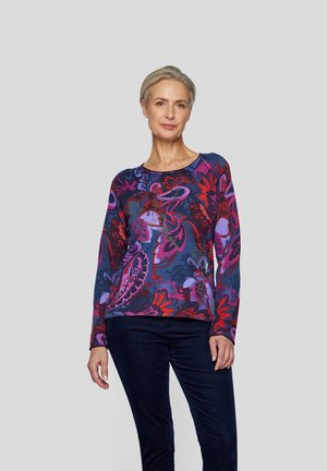 Colorful knit sweater with long sleeves, featuring a floral pattern in purple, red, and blue shades, paired with dark pants.