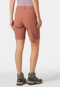 Lekka, rdzawa para spodenek z płaskim pasem i boczną kieszenią, w zestawieniu z szarymi butami trekkingowymi z teksturowanymi detalami i solidną podeszwą.