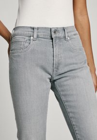 Jeans de mezclilla gris de tiro alto con un diseño clásico de cinco bolsillos, que presentan una cremallera y cierre de botón, y un ligero desvanecimiento para textura.