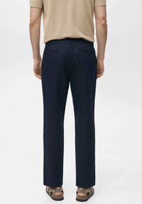 Donkerblauwe broek met een rechte pijp, voorzien van twee achterzakken en een zachte textuur, gecombineerd met bruine sandalen met banden.