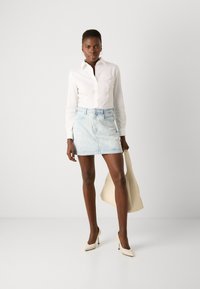 Biela blúzka s dlhými rukávmi, svetlomodrá denim mini sukňa s kvetinovým vzorom, béžová kabelka a krémové lodičky na vysokom opätku. Hladké текстúry po celom oblečení.