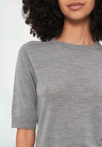 Hall halli lühikeste varrukatega kampsun, millel on ümar kaelus ja mis on valmistatud pehmest, tekstuuriga kangast. Omaduseks on soonikkoes serv ja õmbluste detailid õlgadel.