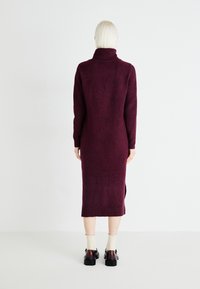 Long, burgundy sweater dress with a high collar, ribbed cuffs, and side slits. Made from soft knit material, extending to mid-calf length.