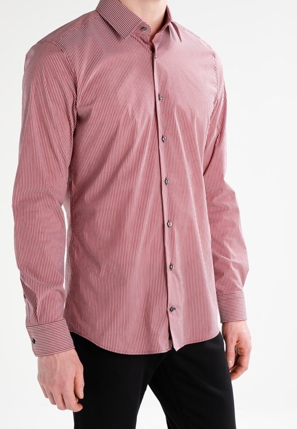 Chemise boutonnée rayée rouge et blanche avec un col, des manches longues et des boutons noirs. Tissu lisse, design ajusté et détails aux poignets.