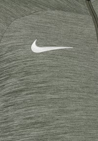 Nike sportjack in olijfgroen, gemaakt van textuurstof, met een opvallend wit logo op de borst en een ritssluiting.
