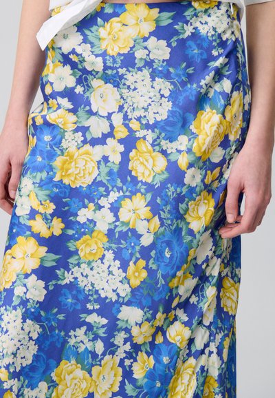 Jupe fleurie en bleu, ornée de fleurs jaunes et blanches. Fabriquée en tissu doux, elle présente un design fluide et une texture subtile.