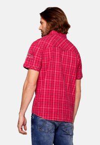Camicia a maniche corte a quadri di un vivace rosso con motivi a scacchi bianchi e neri, caratterizzata da una vestibilità casual e dettagli ricamati sulle spalle.