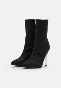 Sorte ankelsko lavet af et strækbart stof, med spidse tæer, et elegant silhuet og en gennemsigtig høj stilettohæl.