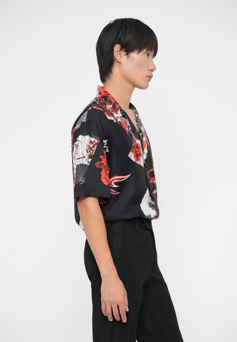 Kurzärmeliges schwarzes Hemd mit roten Blumen- und Fächer-Mustern, ausgestattet mit einem Kragen und einer Knopfleiste, kombiniert mit strukturierten schwarzen Hosen.
