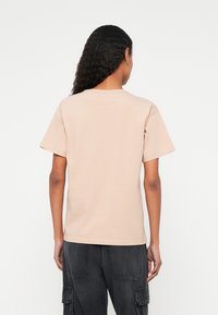 Gaiši persiku kokvilnas T-krekls ar īsām piedurknēm un apaļu izgriezumu, redzams no aizmugures. Gluda tekstūra, bez redzamiem rakstiem vai grafikām.