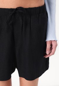Zwarte linnen shorts met een elastische tailleband en trekkoord, met een losse pasvorm en zijzakken, eindigend boven de knie.