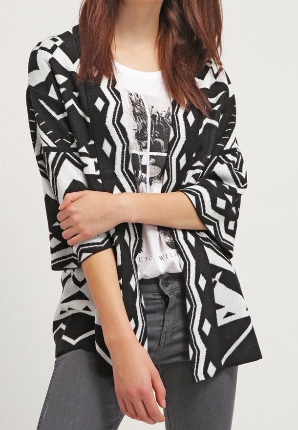 Schwarz-weißer gemusterter Cardigan mit übergroßen Ärmeln, offenem Design und geometrischen Motiven, getragen über einem weißen Grafik-T-Shirt.