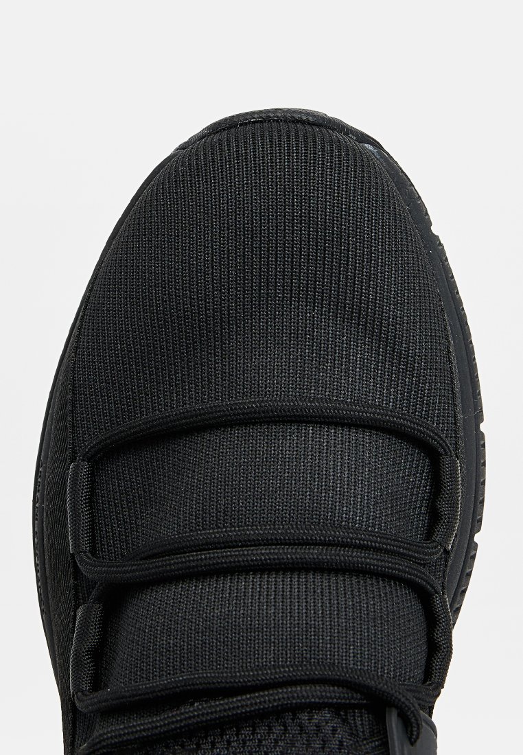 Nahaufnahme der schwarzen Sneaker-Zehenpartie mit Obermaterial aus Strickgewebe und integrierten elastischen Riemen über dem Spann für einen sicheren Sitz.