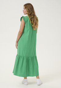 Zelena bombažna maksi obleka s kratkimi naborjenimi rokavi, večplastnim robom in sproščenim krojem, v kombinaciji z belimi športnimi copati.