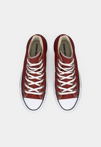 Punased kangast spordijalatsid valgete nööridega, kummist varvasetootega ja kontrastse musta äärega. Sisetalladel on brändi nimi. Ülemise vaate nurk.