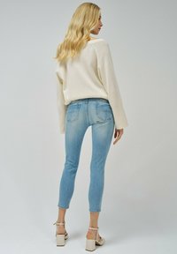 Jeans skiny de denim azul claro, combinados con un suéter crema, que presenta un ajuste relajado y detalles sutiles en los bolsillos.
