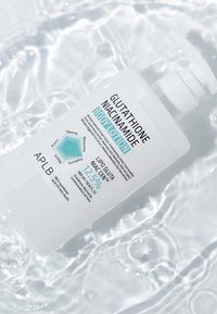 Hvid pumpeflaske med Glutathion Niacinamid bodylotion med 12,5% koncentration, flydende i bølgende klart vand.