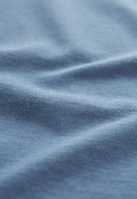 Zbliżenie miękkiej niebieskiej tkaniny pokazującej delikatną dzianą fakturę i łagodne fałdy.