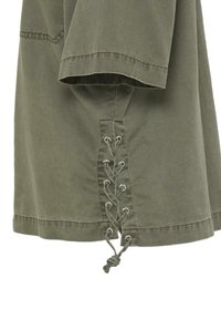 Vêtement en tissu vert avec des manches amples présentant un détail à lacets au niveau de l'ourlet, noué en un nœud avec des œillets métalliques.