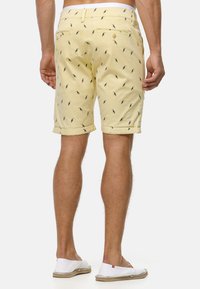 Shorts jaunes en coton avec un motif imprimé de petits oiseaux. Possède des ourlets roulés et des poches arrière avec fermetures à bouton.
