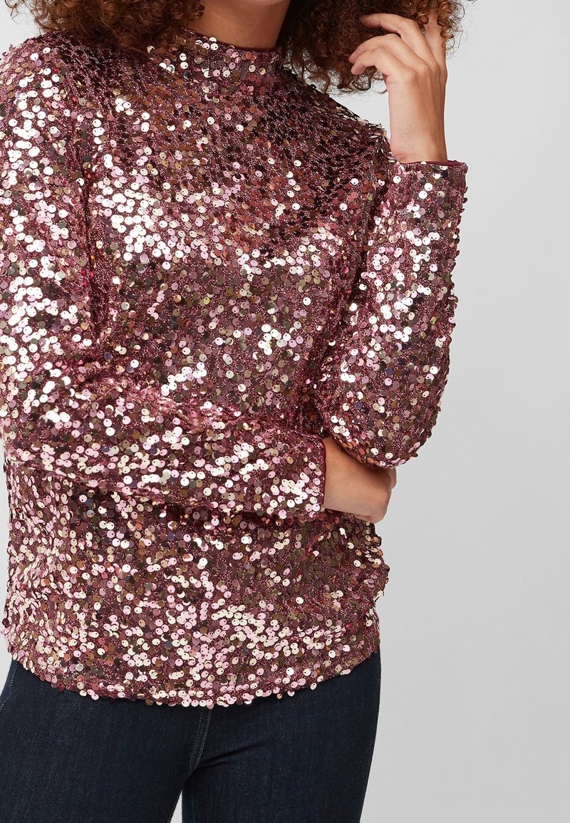 Top a maniche lunghe color oro rosa con paillettes e collo alto. Presenta una silhouette aderente e una superficie lucida e testurizzata grazie alle paillettes.
